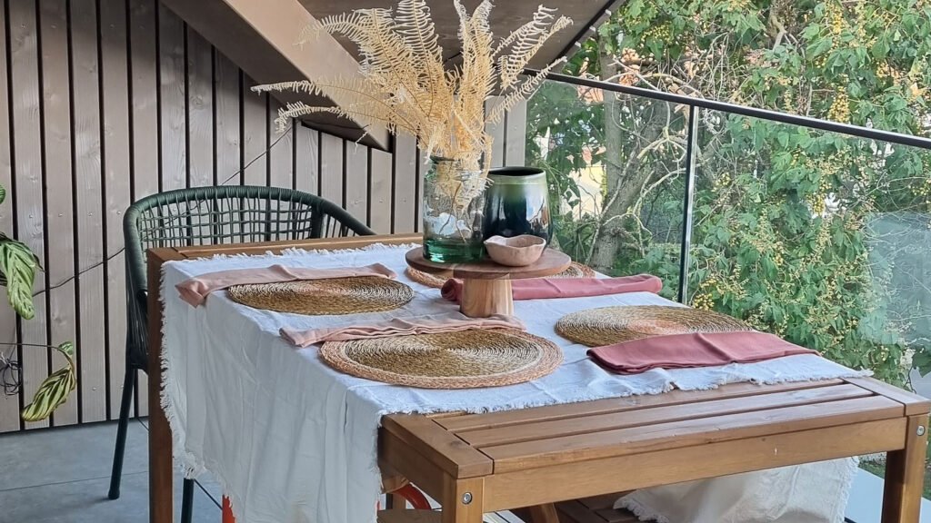 Décoration d'une terrasse avec une table à manger et du linge de maison blanc, vieux rose en matière naturelle.